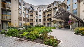 A multi-story building with balconies, a covered entrance, and a landscaped courtyard with various plants.