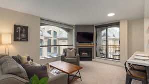A modern living room with a sofa, a coffee table, a fireplace, and large windows offering a view of the neighborhood.