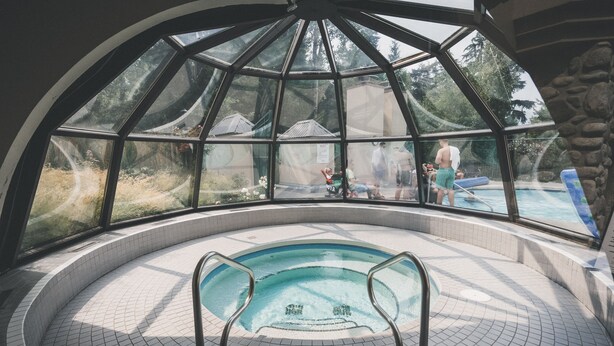 A glass-enclosed hot tub area with a view of a pool and outdoor scenery.