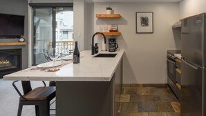 A modern kitchen with a marble countertop, a built-in sink, a coffee maker, and a stainless steel refrigerator.