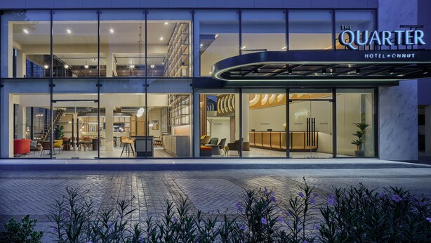 A hotel with a modern design, featuring a glass facade, a reception area, and a visible outdoor seating area. - The Quarter Onnut by UHG (Bangkok)
