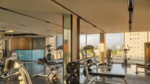 A modern gym with various exercise equipment, large windows, and a reception desk. - The Quarter Onnut by UHG (Bangkok)