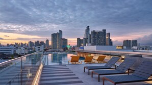 A rooftop pool area with lounge chairs and a city skyline view at dusk. - The Quarter Onnut by UHG (Bangkok)