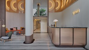 A modern hotel lobby with a reception desk, seating area, and a view of the outdoor space. - The Quarter Onnut by UHG (Bangkok)