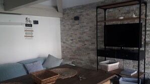 A living room with a sofa, a coffee table, a flat-screen TV on a black stand, and a wall-mounted air conditioner.