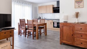A modern kitchen with wooden cabinets, a dining table with chairs, a TV, and a cabinet with a vase. - Apartment `Akazie' in Radolfzell-Liggeringen (Radolfzell am Bodensee)