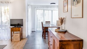 A modern kitchen with wooden cabinets, a dining table, and a TV on a stand. There are two boxes on the floor, possibly for storage or delivery. - Apartment `Akazie' in Radolfzell-Liggeringen (Radolfzell am Bodensee)