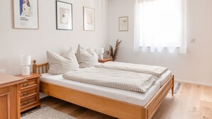 A bedroom with a wooden bed, a nightstand, a lamp, and framed artwork on the wall. - Apartment `Akazie' in Radolfzell-Liggeringen (Radolfzell am Bodensee)