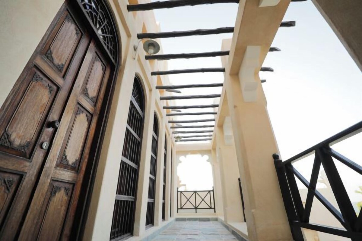 A corridor with a wooden door and windows, leading to a balcony with a railing.