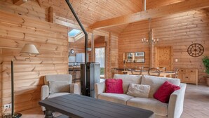 Un accogliente interno di una baita in legno, con zona pranzo, divano con cuscini rossi e un tavolo.
