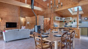 Un'ampia zona giorno con tavolo da pranzo per quattro persone, pareti in legno, camino e cucina dotata di elettrodomestici moderni.