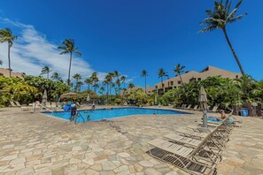 A pool area with lounge chairs, palm trees, and a clear blue sky.