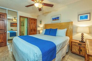 Ein Hotelzimmer mit einem großen Bett, einem Holzkopfende, zwei Nachttischlampen, einem Nachttisch aus Holz und einem Deckenventilator.