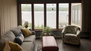 A living room with a large window overlooking a lake, a ceiling fan, and a floral armchair.