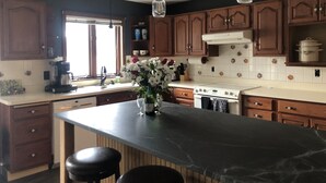 A kitchen with wooden cabinets, a marble island, and pendant lighting.