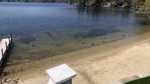 A lake with clear water, a sandy beach, and a dock.
