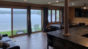 A modern cabin with a large sliding glass door leading to a lake view, a dining area with a stone countertop, and a cozy seating area with a sofa and chairs.