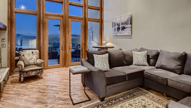 A spacious living room with a large window, a grey sectional sofa, a patterned armchair, and a wooden floor. - Moose on the Loose: Private Hot Tub, Mountain Views, Quick Ski Access (Breckenridge)