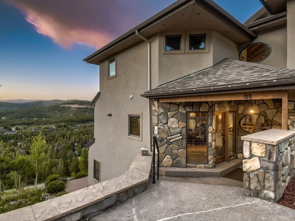 A modern house with a stone facade, a stone patio, and a view of a forested valley.