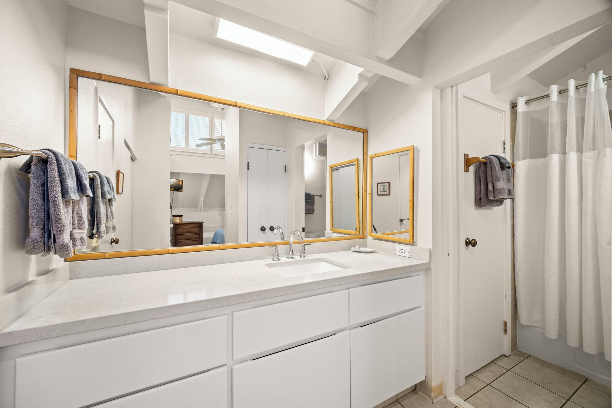 Un baño moderno con un espejo grande, muebles blancos y una zona de ducha.