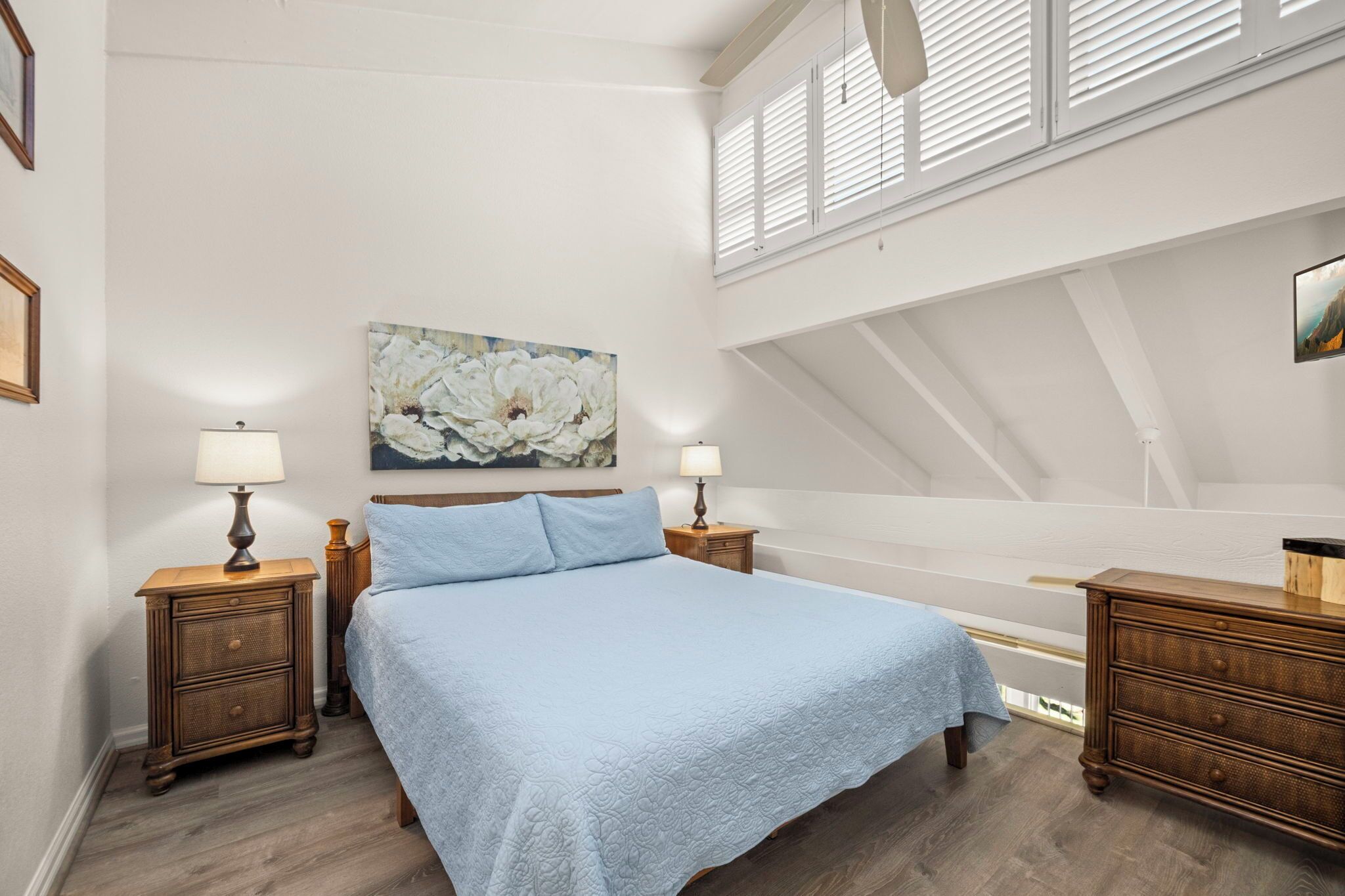 A bedroom with a large bed, two nightstands, a dresser, and a ceiling fan.