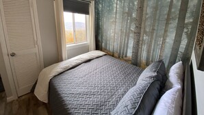 Une chambre à coucher avec un lit, une fenêtre avec des rideaux, une porte et une fresque murale sur le thème de la forêt.