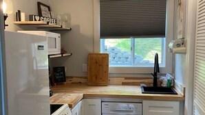 Une cuisine compacte avec des appareils électroménagers blancs, un plan de travail en bois et une fenêtre équipée de stores.