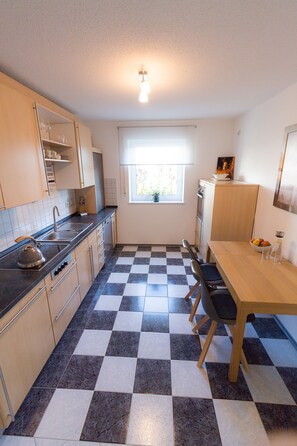 A compact kitchen with a checkered floor, a sink, a kettle, and a dining area with chairs.