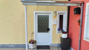 A building entrance with a white door, a small window with a flower box, and a metal awning. - Idyllic vacation apartment near the Ilz for 3 people (Hutthurm)