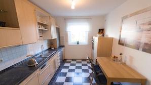 A compact kitchen with a checkered floor, a wooden table, and basic amenities. - Idyllic vacation apartment near the Ilz for 3 people (Hutthurm)