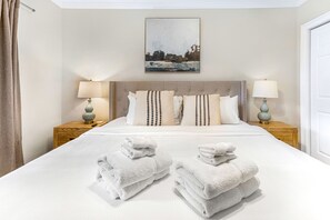 A neatly made bed with white linens and two bedside tables with lamps.