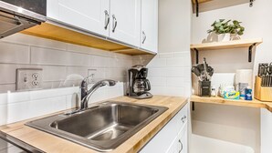 A modern kitchen with a stainless steel sink, wooden countertop, white cabinets, and a coffee maker.