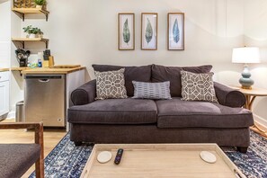 A living room with a gray sofa, patterned pillows, a coffee table, and a remote control.