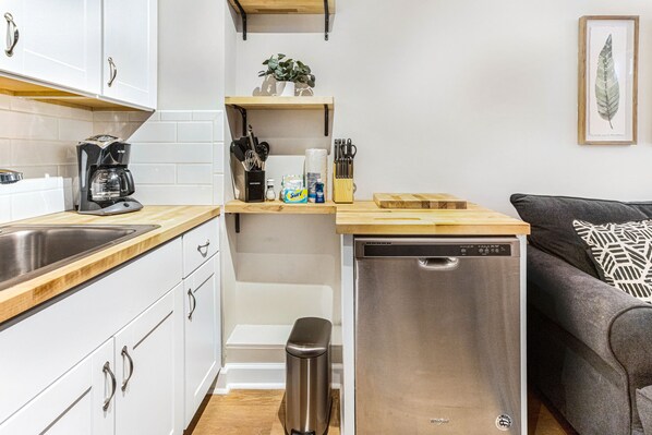 A compact kitchen with a dishwasher, coffee maker, and various utensils on the counter. - Southern Chic Apt. on Forsyth Park w/ Parking, No Stairs by Lucky Savannah (Savannah)