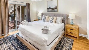 A bedroom with a large bed, two bedside tables with lamps, a ceiling fan, and a sliding glass door leading to an outdoor area.