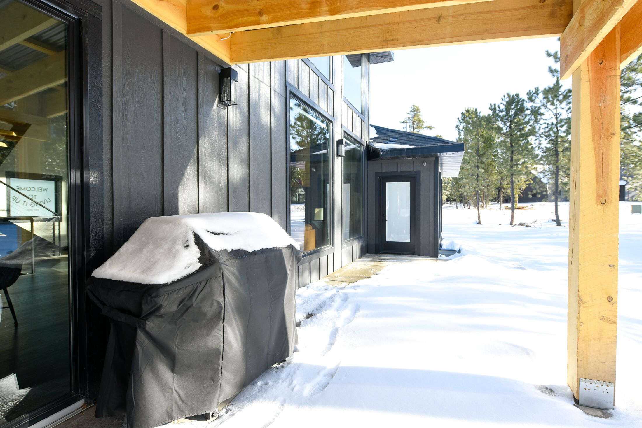 A covered outdoor seating area with a grill, a wooden porch, and a snow-covered ground.