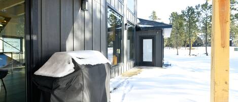A covered outdoor seating area with a grill, a wooden porch, and a snow-covered ground.