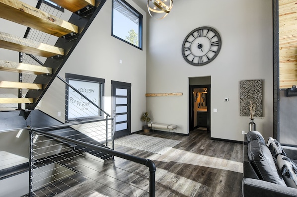 A spacious living area with a staircase, a large wall clock, and a bench.