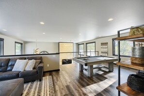 A modern living room with a pool table, leather sofa, and large windows.