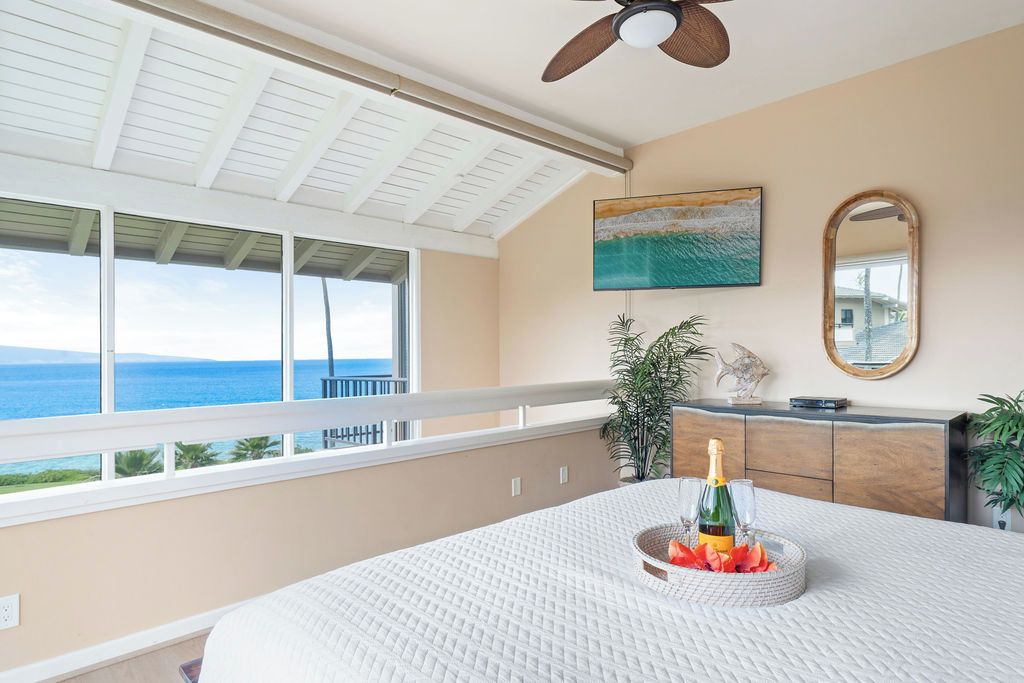 A bedroom with a large window, a ceiling fan, a bed, a nightstand, a mirror, and a painting.