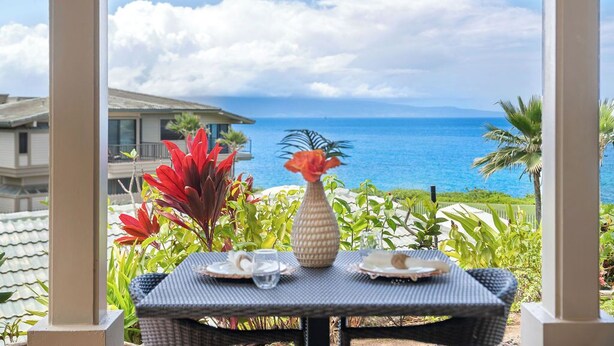 Un espace extérieur abrité, aménagé pour les repas, avec une table pour deux personnes, offrant une vue sur la côte.