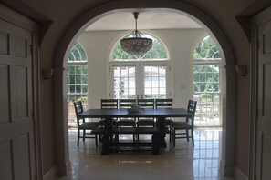 Un comedor con una mesa grande y bancos, un arco de entrada y ventanas amplias con vistas a la vegetación exterior.