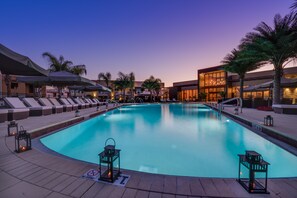 A swimming pool with lounge chairs and umbrellas, surrounded by palm trees and buildings. - Near Disney, Resort Style, Free Parking & Wi-Fi Outdoor shared Pool (Kissimmee)