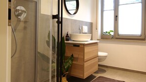 Ein modernes Badezimmer mit einer Duschkabine aus Glas, einem Holzbadezimmerhocker, einem weißen Waschbecken und einem großen Spiegel.