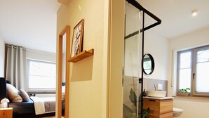 Ein modernes Wohnzimmer mit Sofa, einer Glastrennwand und einem Badezimmer mit Waschbecken und Toilette.
