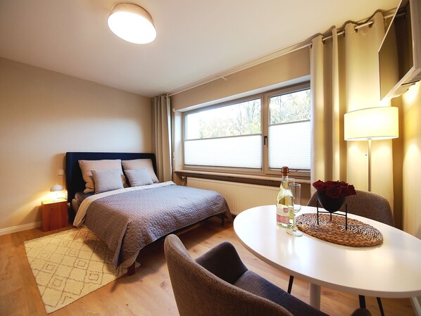 A bedroom with a bed, bedside table, lamp, and a dining area with a table and chairs.