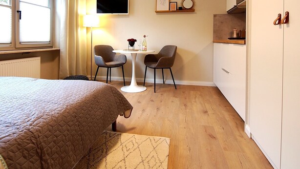 Ein Hotelzimmer mit einem Bett, einem kleinen Esstisch mit Stühlen, einem Fernseher und einer Küchenzeile.