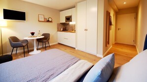 Ein Schlafzimmer mit einem Bett, einem Nachttisch und Stühlen. Es gibt eine Küchenzeile mit einer Mikrowelle und Schränken.