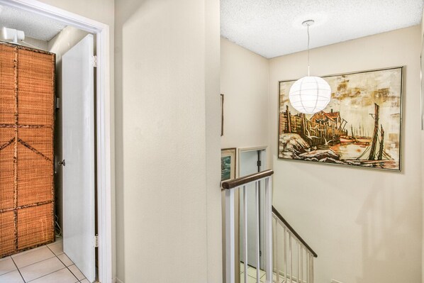 A hallway with a wooden door, a white wall, a painting of a harbor scene, and a white railing.