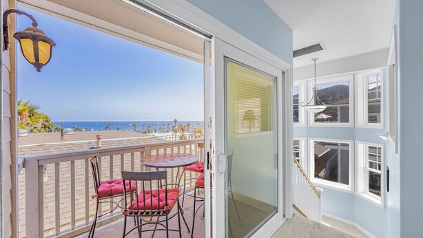 A balcony with a table and chairs, a view of the beach, and a sliding glass door leading to a room with a chandelier. - 217BA: Lovely 3 bdrm, 2.5 Bath, Ocean Views, Wifi (Avalon)